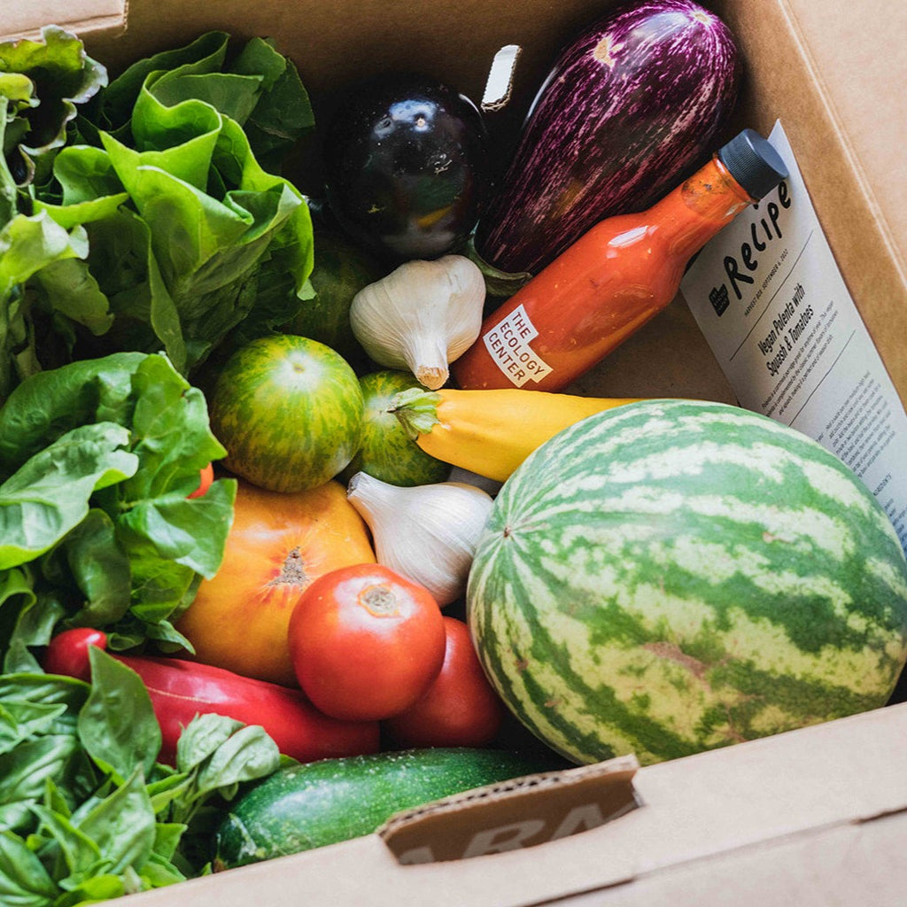 a box full of seasonal vegetables, a recipe card and a pantry item