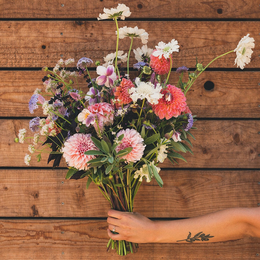 hand holding a big bouquet of seasonal flowers in front of a wood wall background